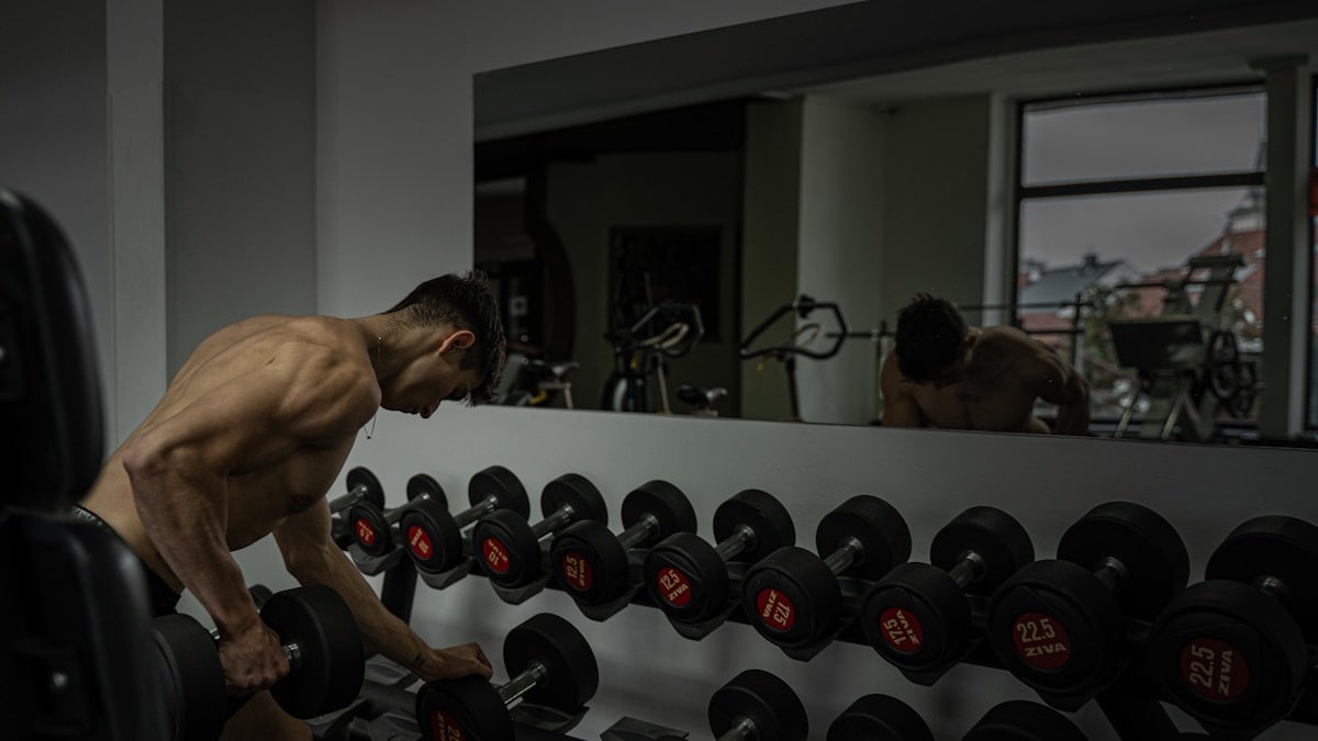 A muscular guy in the gym lifting weights. Doing dumbbell rows in front of a mirror.